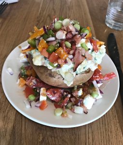 Baked potato on a white plate topped with vegetables and sour cream.