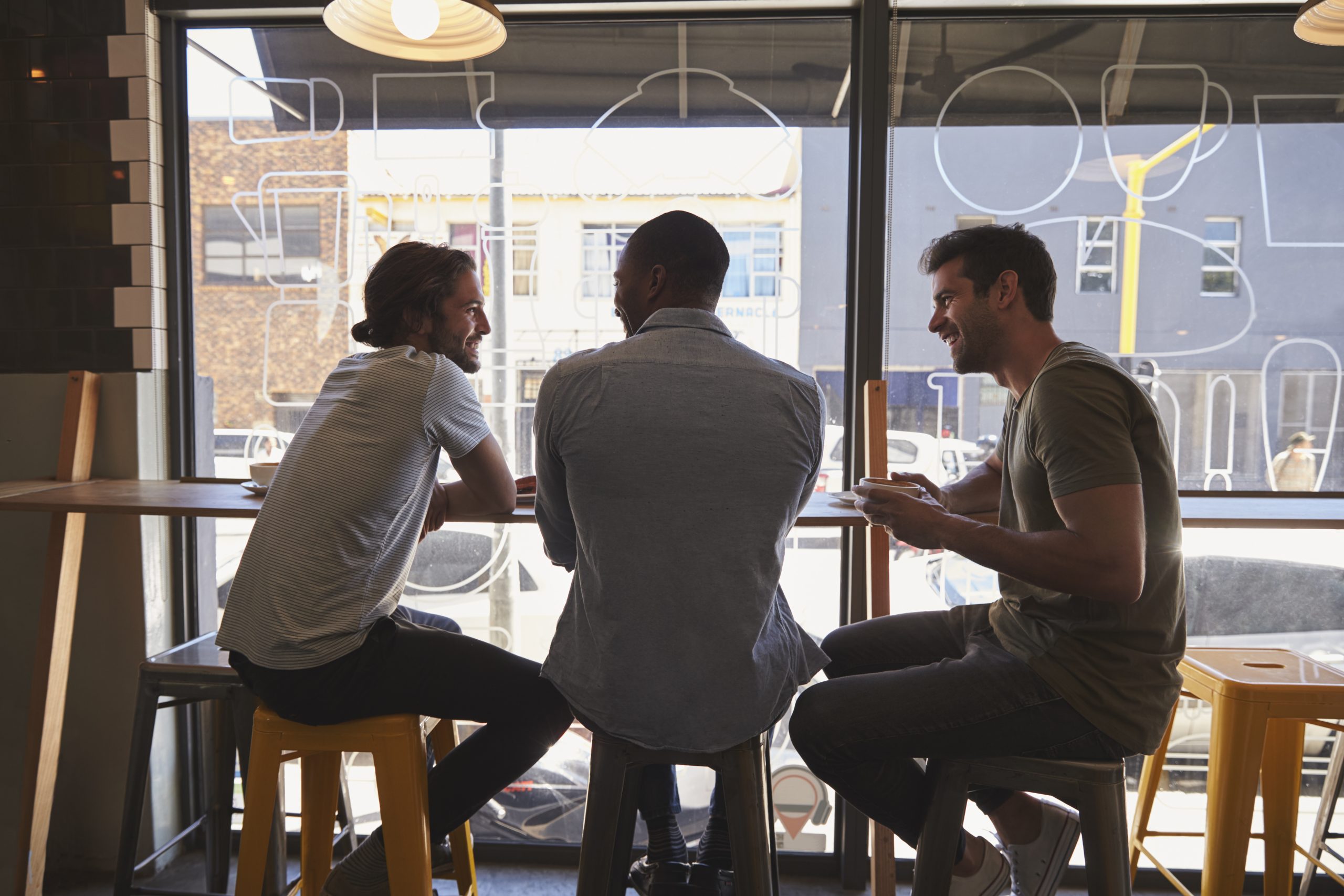 Rear View Of Three Male Friends Meeting In Coffee Shop